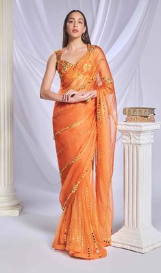 Introducing our vibrant orange organza sari, meticulously crafted from a luxurious blend of organza and tulle. The pallu features intricate gold metallic and acrylic embroidery, forming delicate lines that add elegance. The pre-stitched tulle bottom provides a graceful finish. Complementing the sari is a matching tulle blouse, adorned with abstract gold and chunky embroidery, blending metallic shapes and acrylics for a chic, stylish look. Festive Pre-draped Organza Saree With Gota Work, Gold Organza Pre-draped Saree For Navratri, Gold Organza Pre-draped Saree With Resham Embroidery, Elegant Organza Pre-draped Saree For Navratri, Festive Orange Pre-draped Saree, Bollywood Organza Pre-draped Saree For Eid, Orange Pre-draped Saree With Pallu For Wedding, Orange Pre-draped Saree With Dupatta For Festivals, Orange Pre-draped Saree For Wedding And Diwali