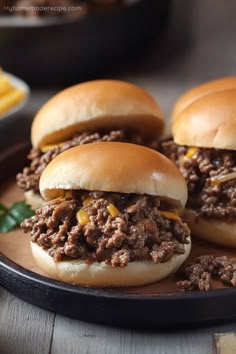 three sloppy joe sliders on a plate with cheese and fries in the back ground