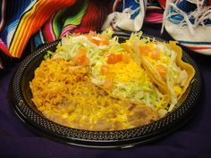 a plate filled with tacos and rice on top of a purple cloth next to shoes