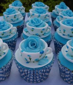 blue cupcakes with white frosting and roses on them sitting on a table