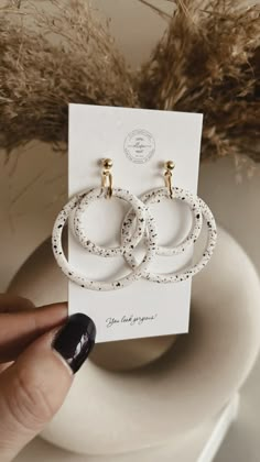 a pair of white earrings sitting on top of a table next to a vase with dry grass