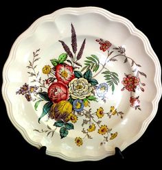 a white plate with flowers painted on the front and sides, sitting against a black background