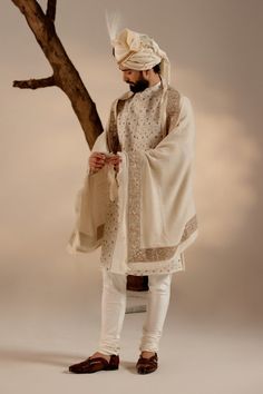 Turtle Dove Sherwani Set | Jatin Malik Introducing our renowned Kashmiri Jamawar embroidered sherwani, crafted in a captivating dirty ivory hue and adorned with intricate floral design details. This masterpiece is further elevated with exquisite dabka and zari work, adding a touch of opulence and refinement. Paired with a matching Ladakhi Pashmina shawl and safa, this ensemble exudes timeless elegance and sophistication, perfect for special occasions and celebrations. With its impeccable craftsmanship and attention to detail, this sherwani set is sure to make a memorable statement. Included in purchase: Sherwani, Kurta, Churidar, Pashmina Shawl, Safa Product Specification Color: White Fabric: Linen silk Occasion: Engagement, Wedding, Bridal, Reception Style: Sherwani, Kurta, Churidar, Pash Eid Bandhgala With Chikankari Embroidery In Jamawar, Off White Bandhgala With Naqshi For Festive Occasions, Off White Naqshi Bandhgala For Festive Occasions, Festive Off White Bandhgala With Naqshi, Ceremonial Churidar With Naqshi Straight Kurta, Cream Sherwani With Chikankari Embroidery And Long Sleeves, Traditional Jamawar Churidar With Naqshi Detailing, Cream Long Sleeve Sherwani With Chikankari Embroidery, Jamawar Churidar With Naqshi And Traditional Drape