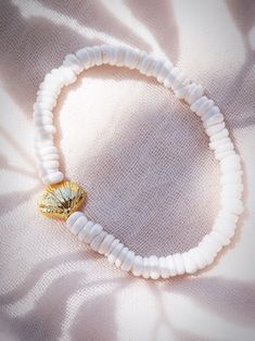 a white beaded bracelet with a gold heart charm on it's end, sitting on a light colored fabric