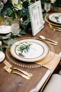 the table is set with gold and white plates, silverware, and greenery