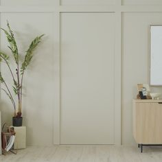 an empty room with white walls and a wooden cabinet next to a potted plant