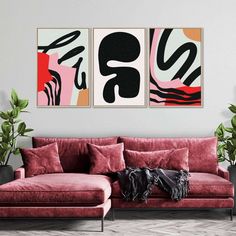 two abstract paintings hang on the wall above a red couch in front of a potted plant