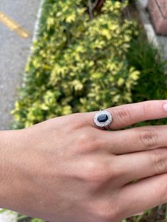 a woman's hand with a ring on it and a plant in the background