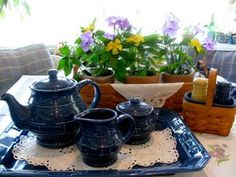 a tray with three teapots on it and some flowers in the back ground