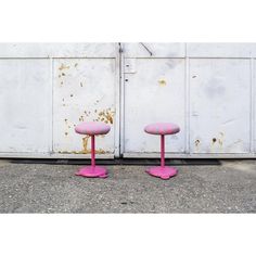 two pink stools sitting next to each other in front of a white wall with peeling paint