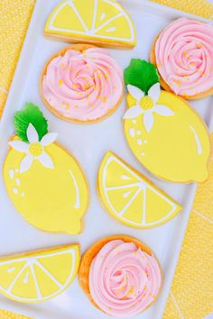 lemon cookies decorated with pink icing and oranges on a white platter next to a yellow towel