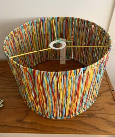 a basket made out of strips of paper on top of a wooden table next to a plant