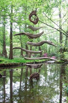 an artistic sculpture in the middle of a pond surrounded by trees and grass with water running through it