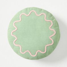 a green round pillow with pink thread on the bottom and an embroidered scalloped edge