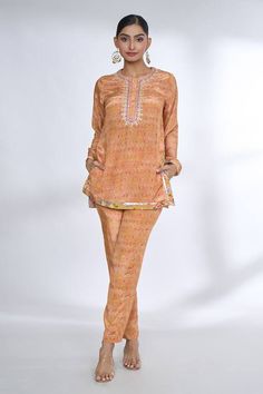 Orange short tunic style top with multi colored prints with embroidered neckline and placet. Comes with coordinating printed pant. - Aza Fashions Eid Long Sleeve Sets With Embroidered Neckline, Long Sleeve Sets With Embroidered Neckline For Eid, Eid Sets With Embroidered Neckline And Long Sleeves, Eid Tunic Set With Embroidered Neckline, Silk Set With Embroidered Neckline And Straight Kurta, Straight Kurta Sets With Printed Motifs For Work, Printed Motifs Tunic Set, Workwear Sets With Printed Motifs And Straight Kurta, Festive Tunic Sets With Embroidered Neckline