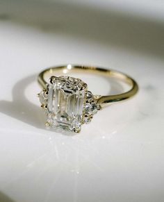 an emerald cut diamond ring on a white surface