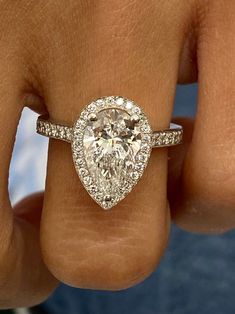 a close up of a person's hand holding a ring with a pear shaped diamond