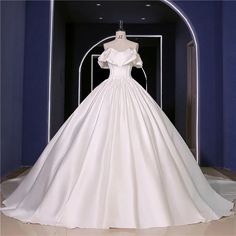 a white wedding dress on display in front of a blue wall with an arched doorway