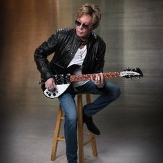 a man sitting on top of a stool holding an electric guitar in his right hand