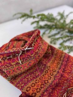 an orange and red scarf sitting on top of a white table next to a plant