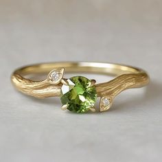 a gold ring with a green stone and two diamonds on the side, sitting on a white surface