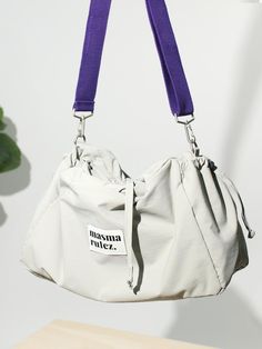 a white purse with purple straps hanging from it's side, next to a potted plant