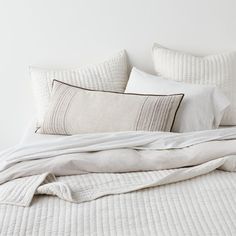 an unmade bed with two pillows and blankets on top of it, next to a white wall