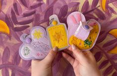 a person holding three small tags in their hands on a purple background with yellow and pink flowers