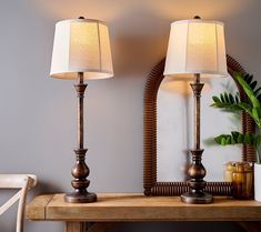 two lamps sitting on top of a wooden table next to a mirror and potted plant