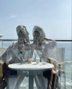 two women sitting at a table with their cell phones in front of them, both wearing headscarves