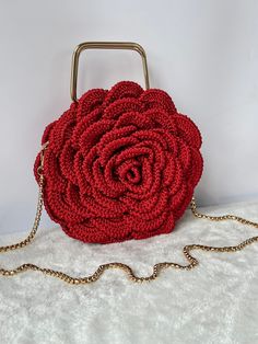 a red crocheted rose purse on a white blanket with a chain around it