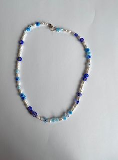 Introducing our stunning handmade beaded necklace, featuring beautiful look-alike water pearls and blue millefiori beads for a touch of elegance and style. This necklace is perfect for dressing up any outfit or adding a pop of color to your everyday look. The crewneck style sits comfortably around your neck, making it a versatile piece that you'll love to wear time and time again. 💙 CARE INSTRUCTIONS: Please handle with care and avoid exposing to water or harsh chemicals to ensure the longevity Summer Blue Necklaces With Spacer Beads, Blue Pearl Beach Jewelry, Blue Round Beads Necklaces For Summer, Handmade Blue Necklace For Summer, Summer Blue Beaded Necklaces With Letter Beads, Blue Pearl Necklaces For The Beach, Blue Pearl Necklaces For Beach, Blue Letter Beads Necklace For Summer, Blue Bohemian Pearl Necklaces