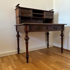 an old wooden desk sitting on top of a hard wood floor next to a white wall