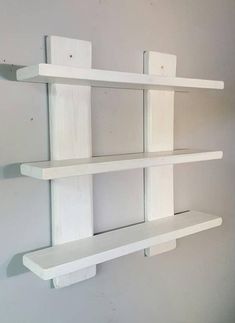 two white shelves are on the wall with one shelf holding three different pieces of wood