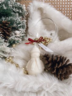 a wine glass and pine cones on a white fur covered surface with christmas decorations in the background