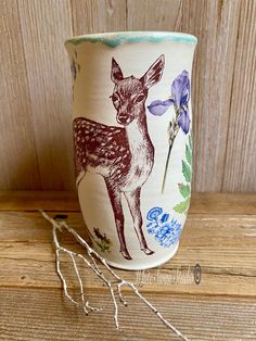 a ceramic cup with an image of a deer on it sitting on a wooden table