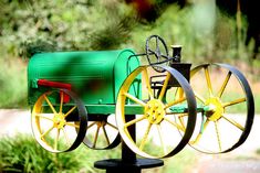 a green and red toy train sitting on top of a wooden rail next to trees