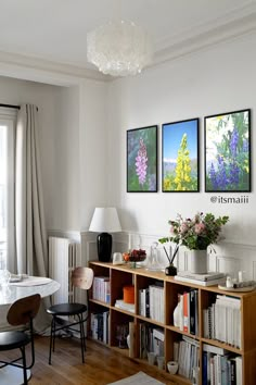 a dining room table and chairs in front of a bookshelf with pictures on the wall