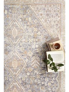 an area rug with a book, cup and plant on the floor next to it