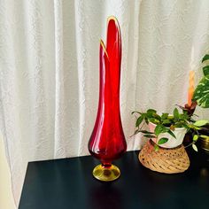 a red vase sitting on top of a black table next to a potted plant