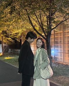 a man and woman standing next to each other in front of a tree at night