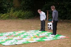 two young men standing on top of a green and white blanket in the grass next to each other