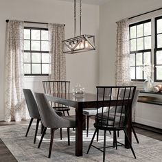 a dinning room table with chairs and a rug in front of the dining room windows