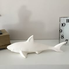 a white shark figurine sitting on top of a table next to a clock