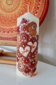 a white candle with hearts on it sitting next to a red and gold plated painting