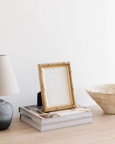 a table topped with books and a gold framed photo next to a lamp on top of a wooden table