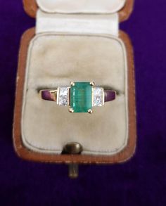 Beautiful pre-loved ring set with an emerald cut emerald flanked by 2 princess cut diamonds. The diamonds are all bright and sparkly, perfectly complimenting the emerald. The emerald is a mid-green colour, it has some natural inclusions typical for an emerald.  Emerald gemstones were mined in Egypt as early as 330 BC, but some estimate that the oldest emeralds are 2.97 billion years old. Cleopatra is perhaps the most famous historical figure to cherish emerald gemstones. She even claimed ownersh Classic Princess Cut Emerald Ring With Diamond Detail, Princess Cut Emerald Ring In Yellow Gold, Heirloom Three Stone Emerald Cut Emerald Ring, Classic Emerald Princess Cut Diamond Ring, Classic Princess Cut Emerald Diamond Ring, Emerald Princess Cut Ring With Center Stone, Square Cut Emerald Diamond Ring For Anniversary, Formal Princess Cut Emerald Ring, Fine Jewelry Green Princess Cut Diamond Ring