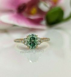 a close up view of a green and white diamond ring on a table with flowers in the background