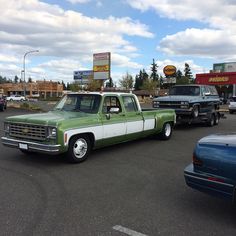 a green and white pickup truck parked in a parking lot next to other cars on a cloudy day