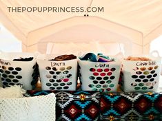 four white buckets filled with personalized items sitting on top of a couch under a tent